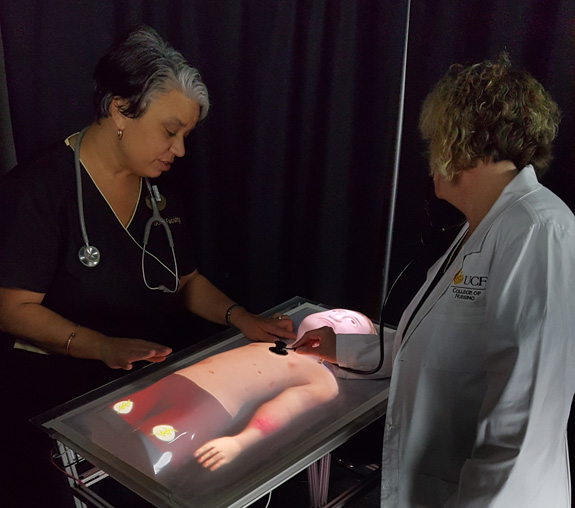 Desiree Diaz and Mindi Anderson with pediatric physical-virtual patient bed.