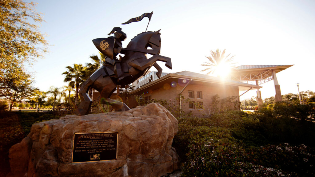 A statue of a UCF Knight riding a horse outside the UCF Fairwinds Alumni Center with the sun glaring on the roof