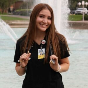 Erin Tonkin, a senior nursing student at the University of Central Florida, in nursing scrubs holding a stethoscope in front of the university reflecting pond