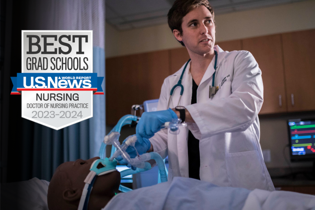 UCF College of Nursing student in a white coat in simulation lab with U.S. News Best Grad Schools Nursing, Doctor of Nursing Practice 2023-2024 badge