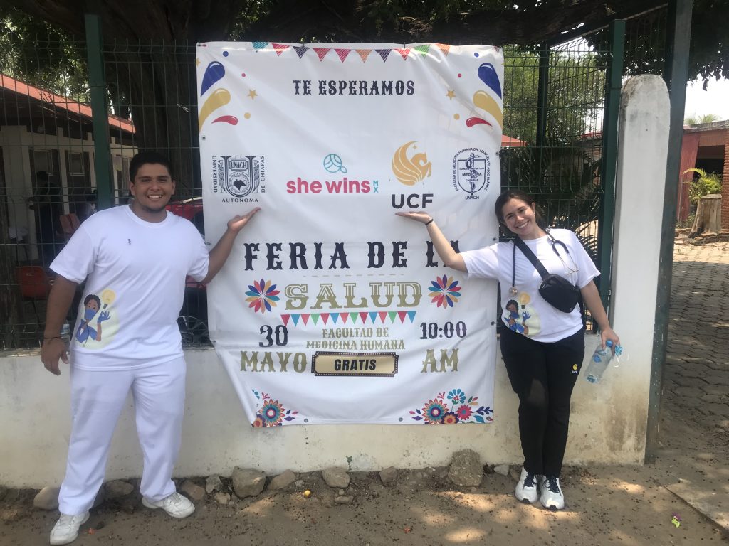A UCF nursing student and a UNACH medical student in front of a health fair sign in Chiapas, Mexico