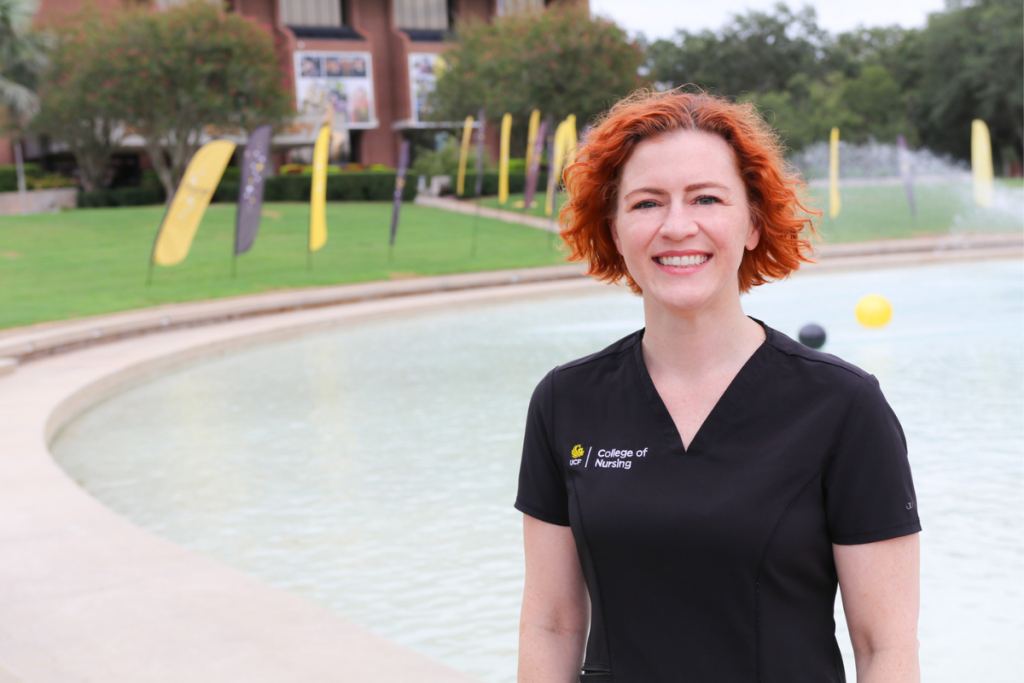 UCF nursing student Kris Hysler in front of the reflecting pond with graduation flags along the edge.