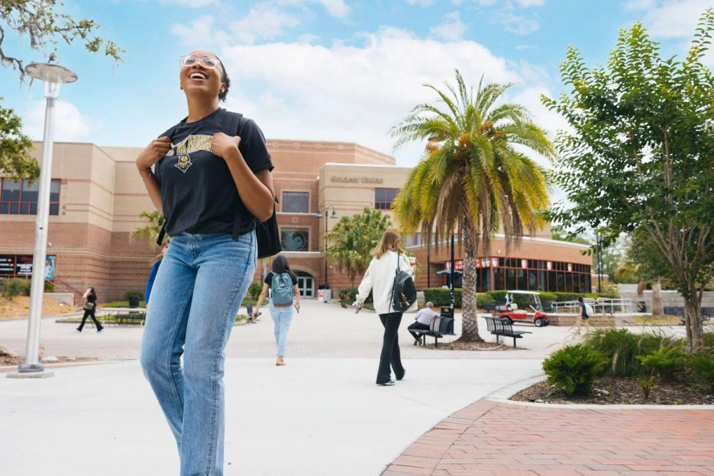 A female student in a UCF Knights t-shirt and jeans walks in front of the Student Union on the UCF campus in Orlando, Florida