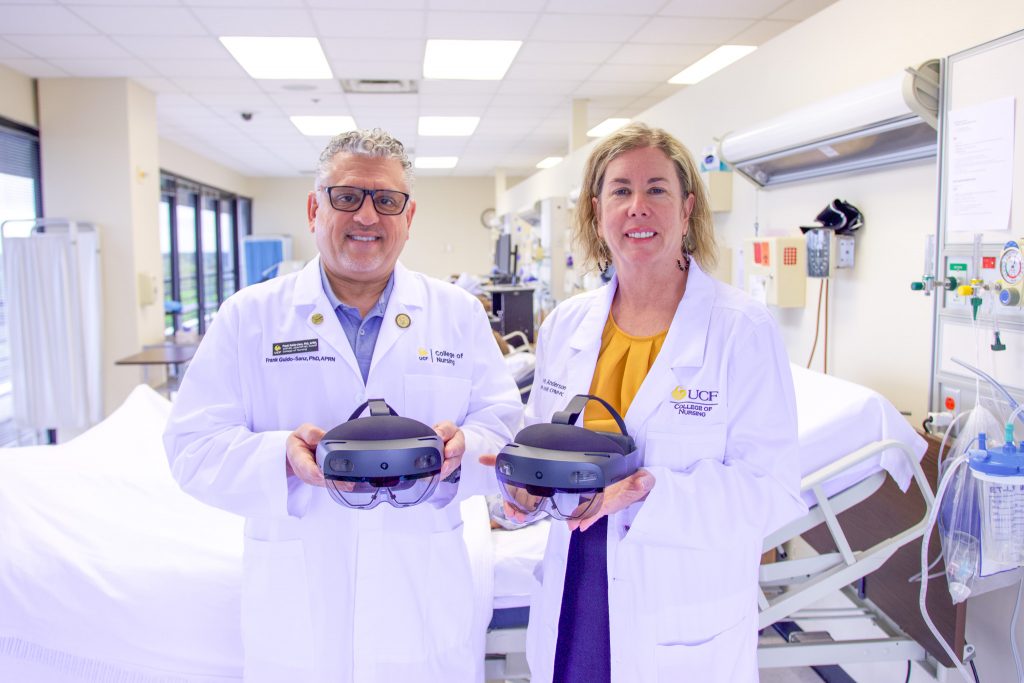 UCF College of Nursing faculty members Frank Guido-Sanz and Mindi Anderson wearing white clinical coats holding VR heads in a simulation learning lab.
