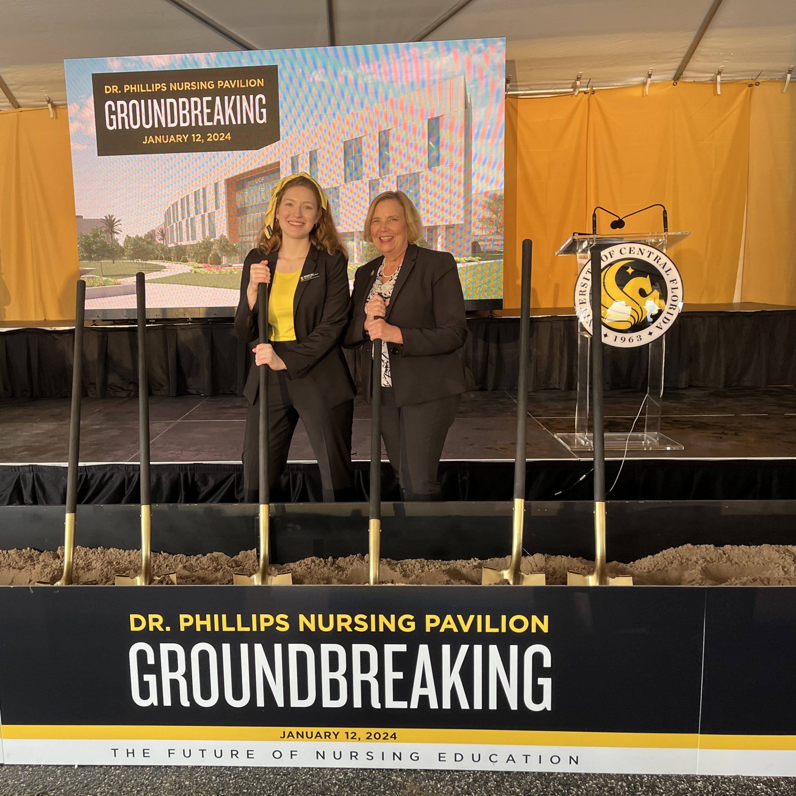 Rebekah May and Dean Sole with shovels in front of signage for the Dr. Phillips Nursing Pavilion Groundbreaking.