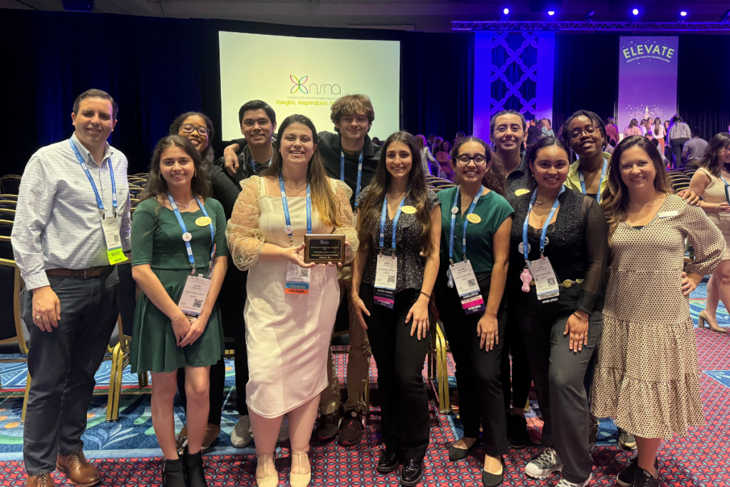 Student Nurses' Association at UCF Orlando board members and faculty advisers stand with NSNA Stellar Chapter plaque inside a ballroom