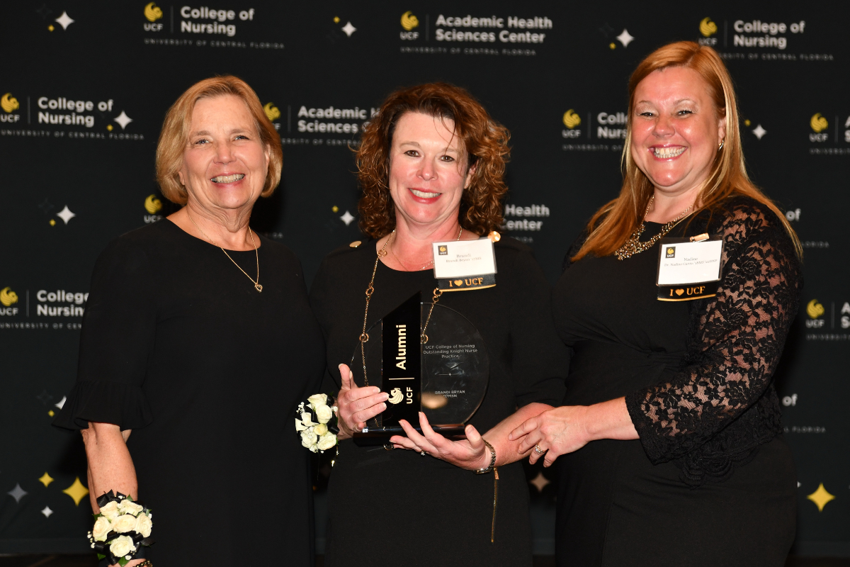 2023 Outstanding Knight Nurse Awardee Brandi Bryan holds a glass award and stands between UCF College of Nursing Dean Mary Lou Sole and UCF College of Nursing Alumni Chapter board member Nadine Garcia.