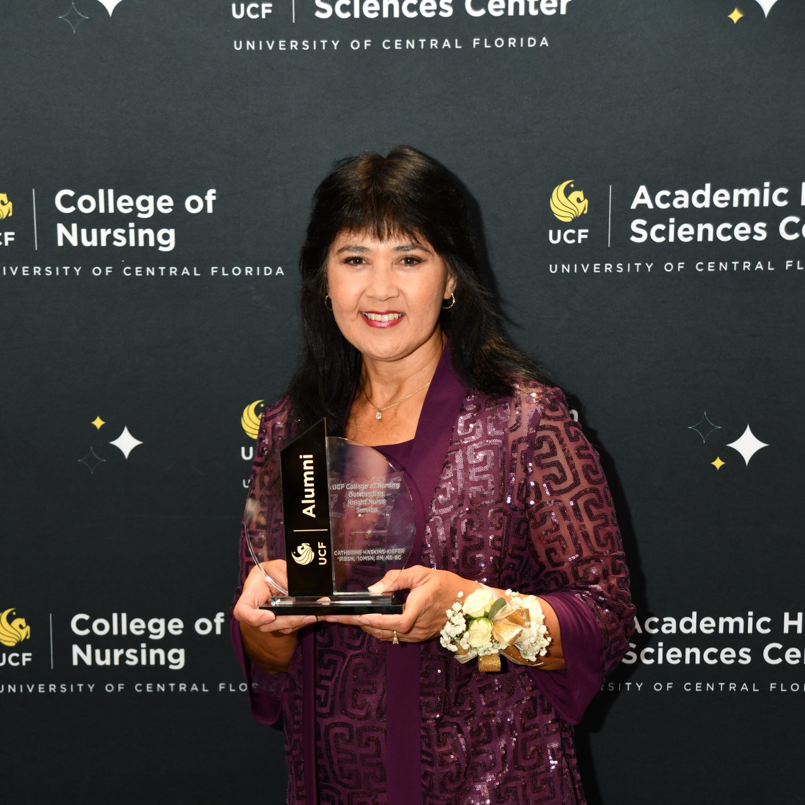 Catherine Haskins-Kiefer holding a crystal UCF Alumni award in front of a UCF College of Nursing banner