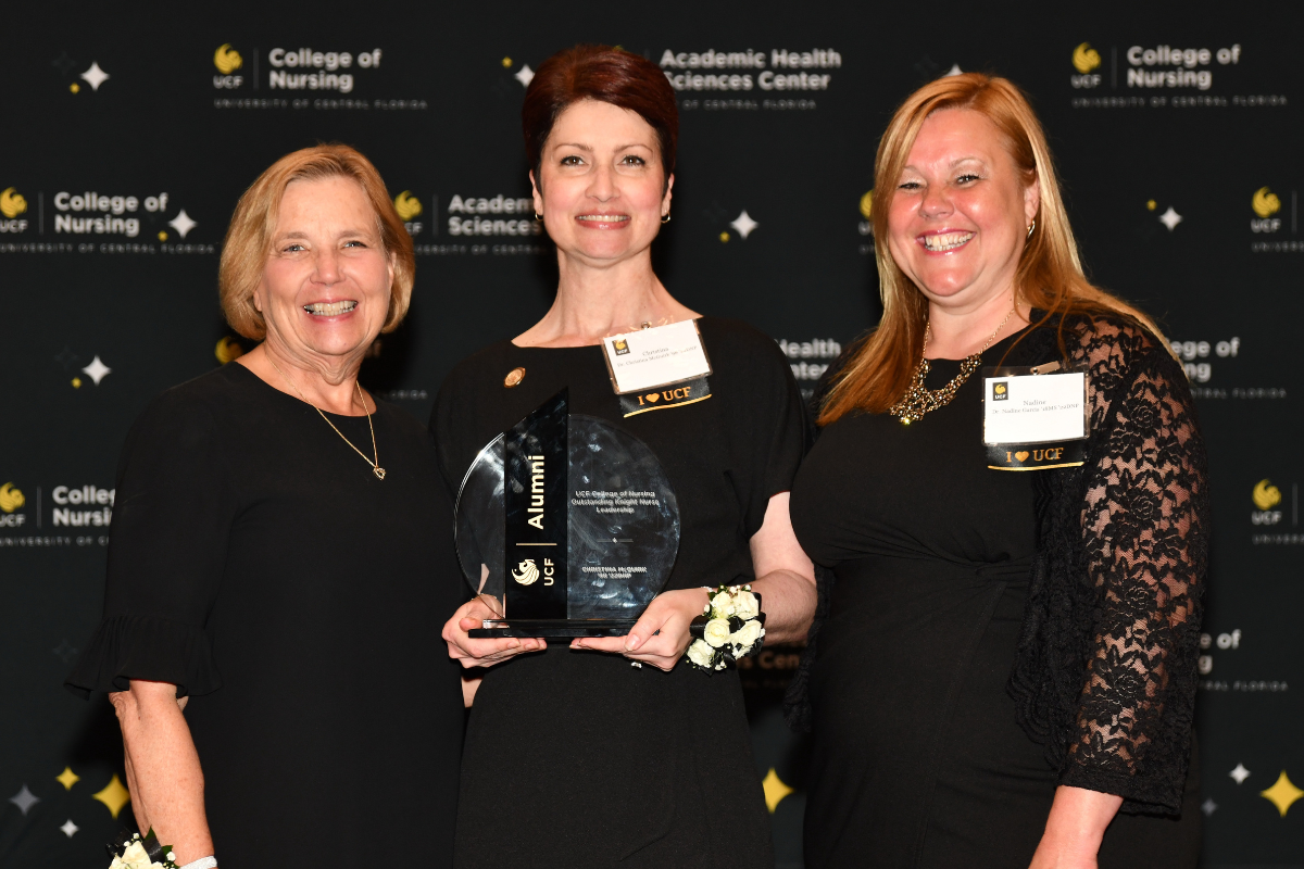 2023 Outstanding Knight Nurse Awardee Christina McGuirk holds a glass award and stands between UCF College of Nursing Dean Mary Lou Sole and UCF College of Nursing Alumni Chapter board member Nadine Garcia.