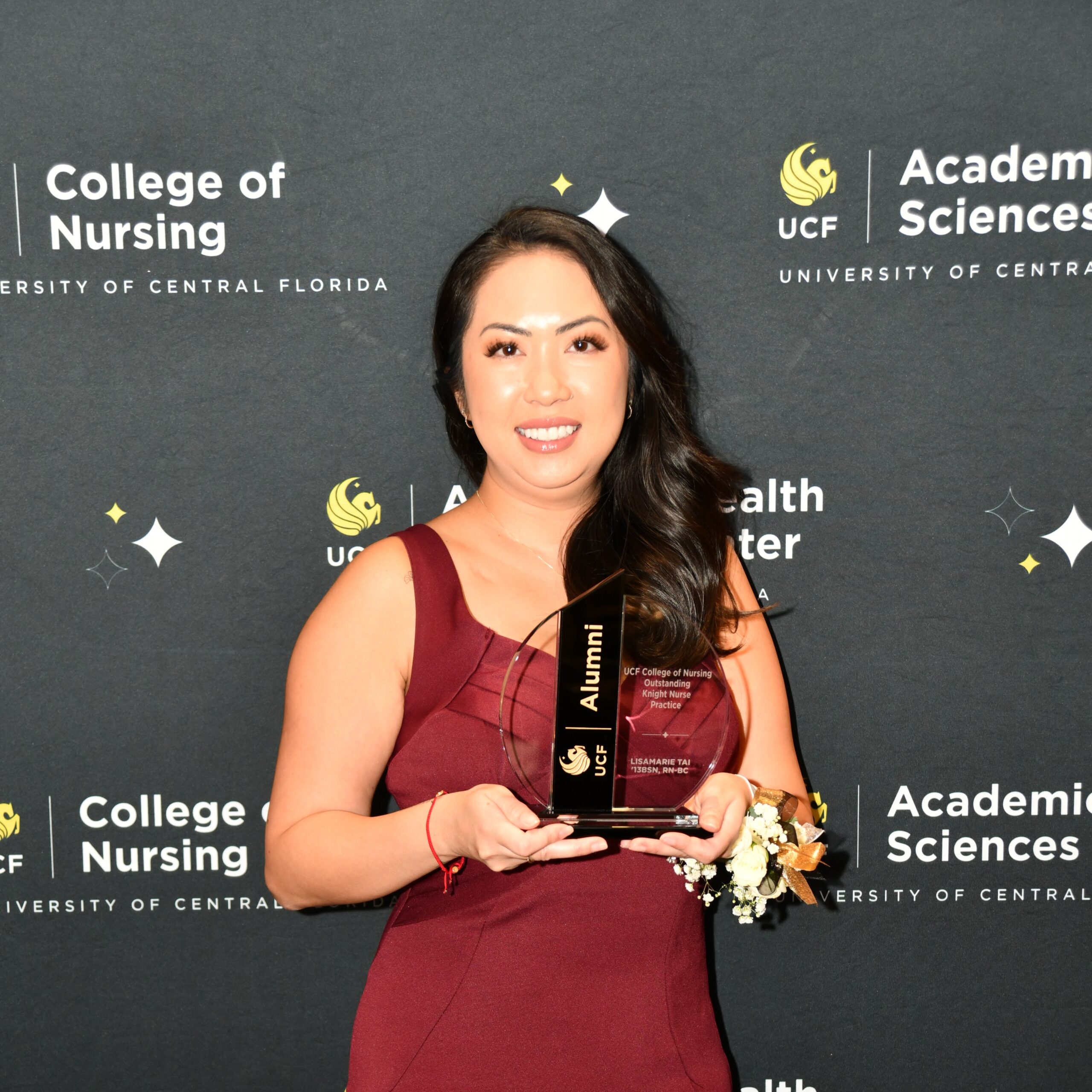 Lisamarie Tai holding a crystal UCF Alumni award in front of a UCF College of Nursing banner