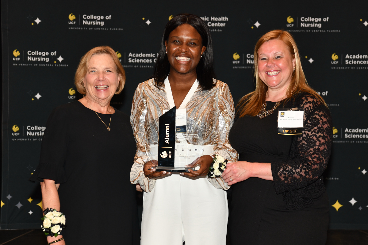 2023 Outstanding Knight Nurse Awardee Marie Smith-East holds a glass award and stands between UCF College of Nursing Dean Mary Lou Sole and UCF College of Nursing Alumni Chapter board member Nadine Garcia.