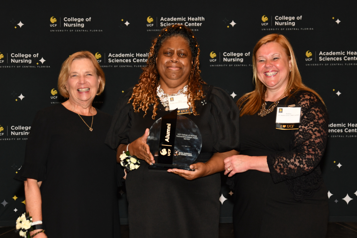 2023 Outstanding Knight Nurse Awardee Myra Sherman holds a glass award and stands between UCF College of Nursing Dean Mary Lou Sole and UCF College of Nursing Alumni Chapter board member Nadine Garcia.