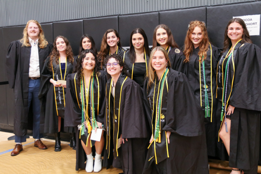 A large group of UCF nursing students from the Cocoa campus smile in regalia inside an auditorium
