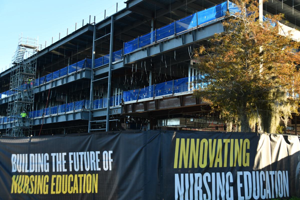 A look at ground level of the construction structure of the Dr. Phillips Nursing Pavilion with a UCF Innovating Nursing Education banner in front.