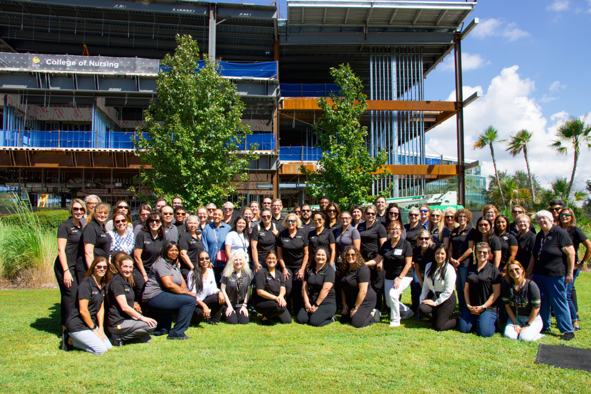 A large group of UCF faculty and staff pose outside the Dr. Phillips Nursing Pavilion, which is under construction, on a sunny day in Florida.