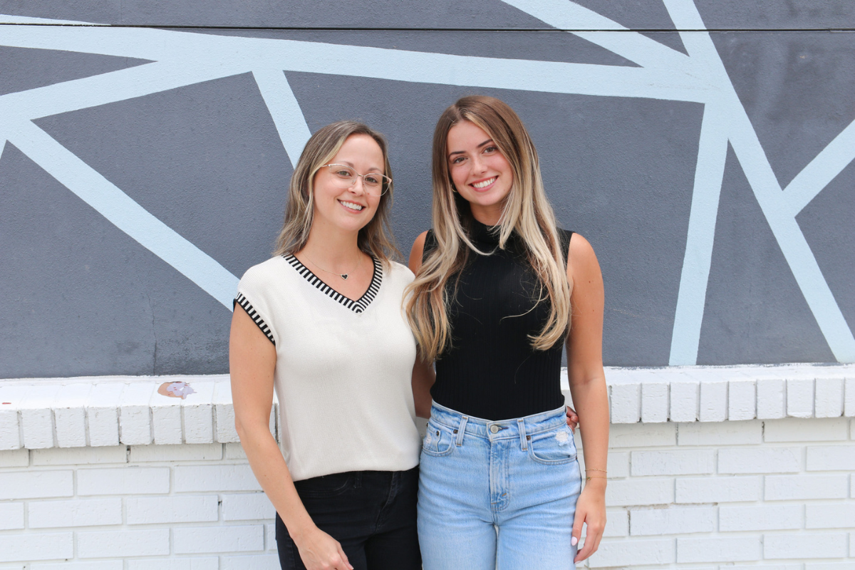 Two UCF College of Nursing alumni, a mentor and mentee, stand in front of a geometric patterned wall outside.