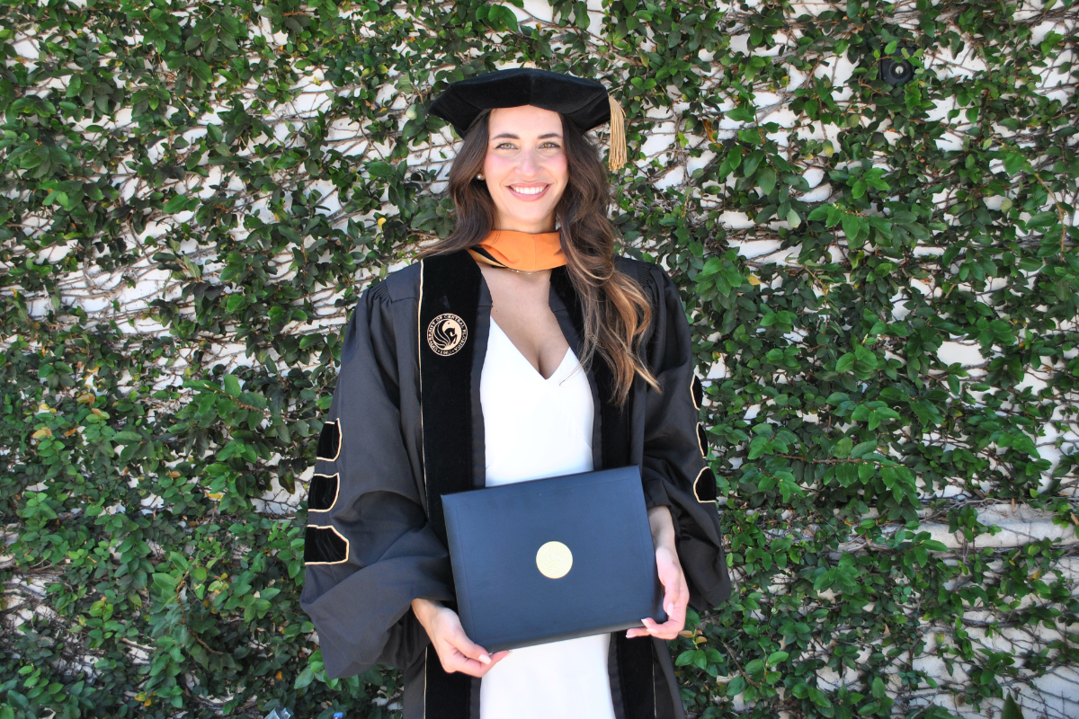 Summer 2024 Family Nurse Practitioner Doctor of Nursing Practice graduate Kaitlyn Hall '18BSN stands outside holding a degree plaque wearing a cap and gown with UCF pegasus logo