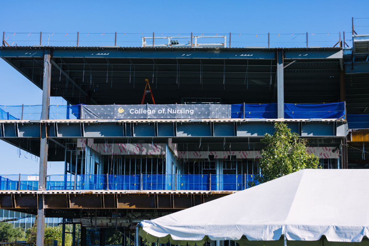 A look up at the structural framing of the Dr. Phillips Nursing Pavilion with a UCF College of Nursing banner hanging from the second floor on a clear sunny day in Florida