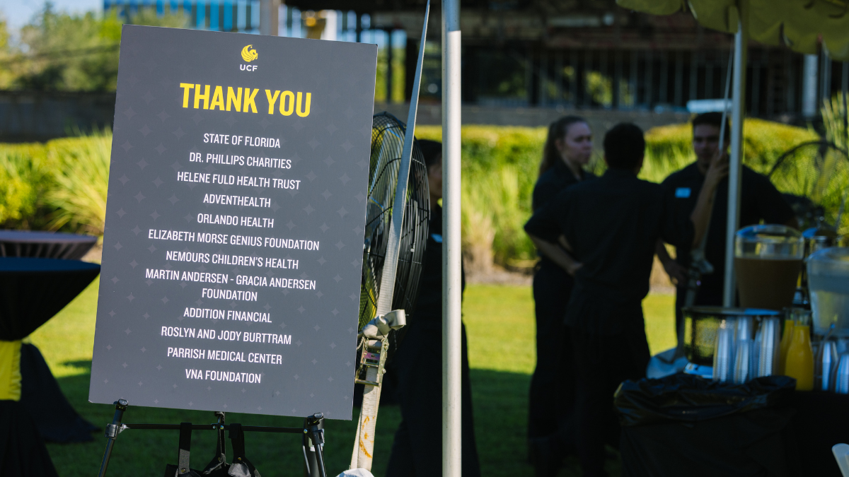 A list of donors on a UCF Thank You poster sits on an easel in front an event tent