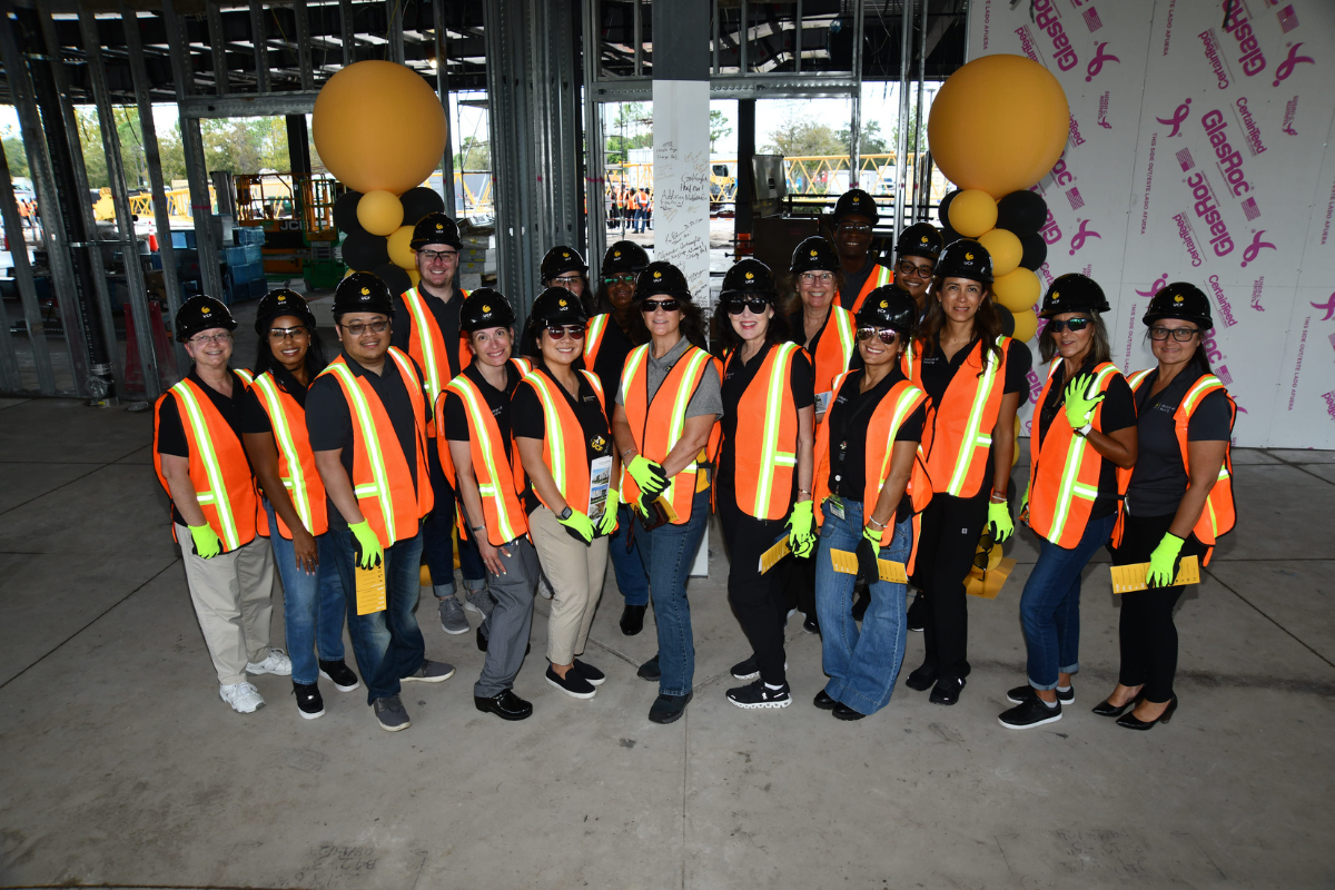 A group of UCF faculty and staff wearing construction vests, gloves and hard hats pose in front of balloons and a steel column inside the Dr. Phillips Nursing Pavilion, which is under construction in Orlando, Florida