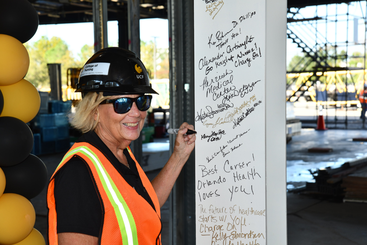 UCF College of Nursing Dean Mary Lou Sole, wearing a construction vest and hard hat, smiles as she signs a steel beam inside the Dr. Phillips Nursing Pavilion, which is under construction.