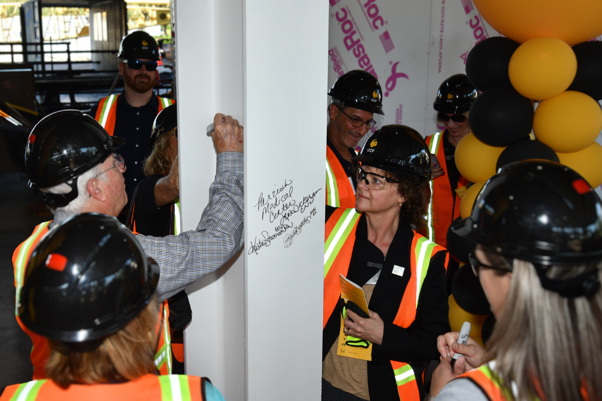 A group of donors wearing construction vests, gloves and hard hats sign the final beam inside the Dr. Phillips Nursing Pavilion, which is under construction in Orlando, Florida.