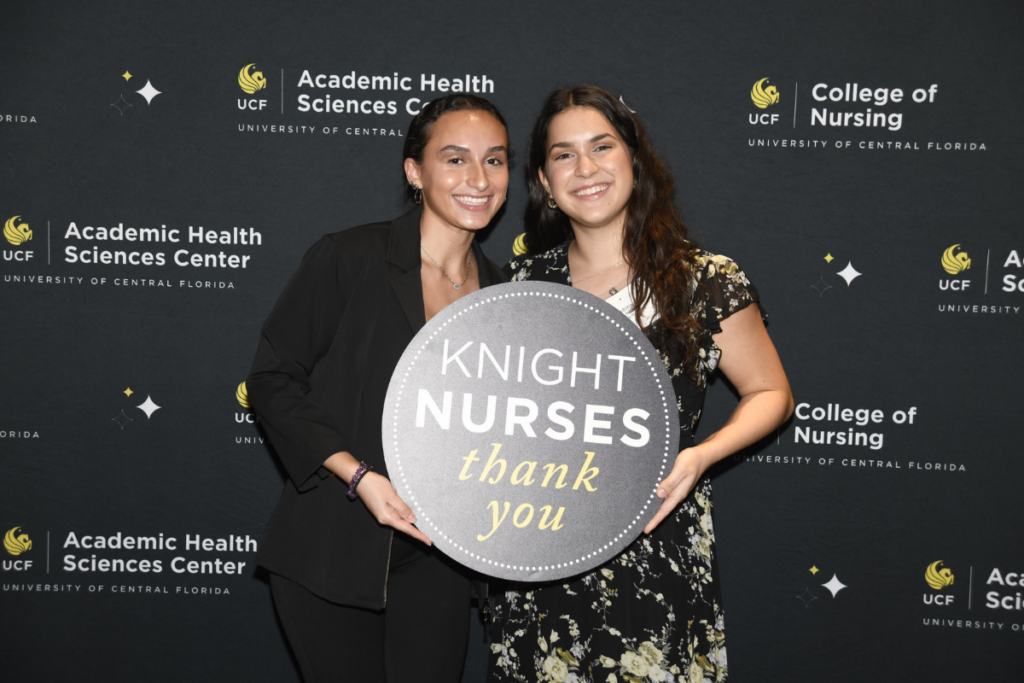 Two UCF College of Nursing students hold a sign that says Knight Nurses Thank You in front a UCF banner