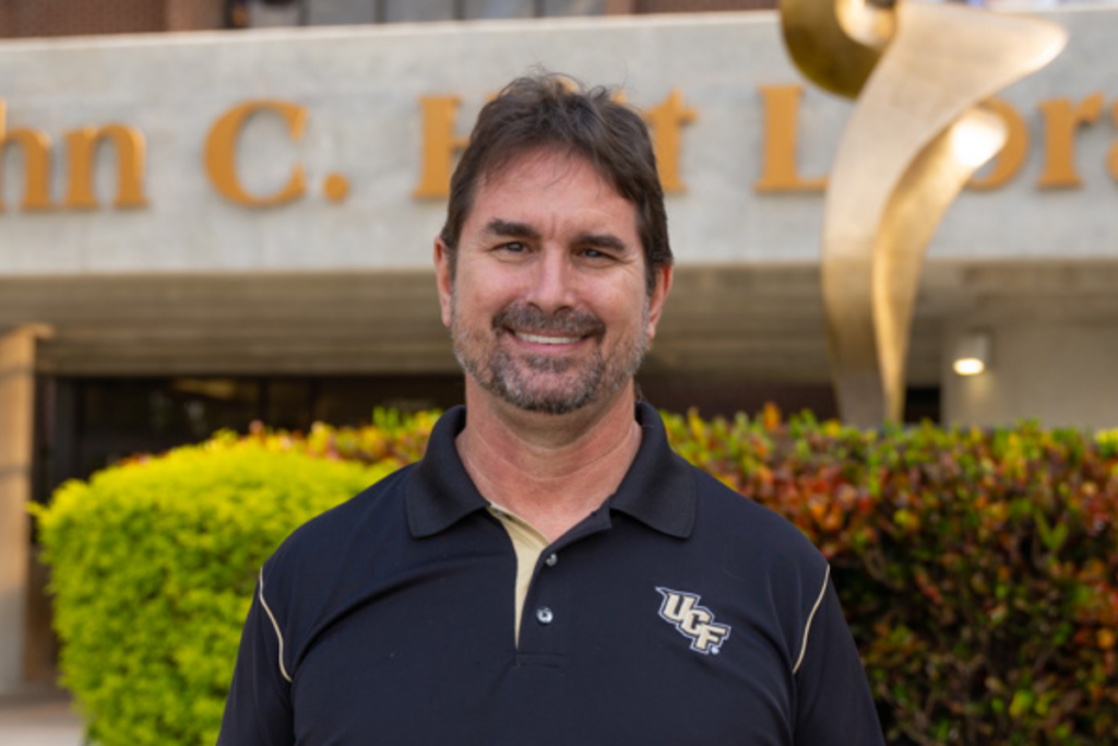 Subject Librarian for the UCF College of Nursing Andrew Todd smiles outside in front of the John C. Hitt Library at UCF