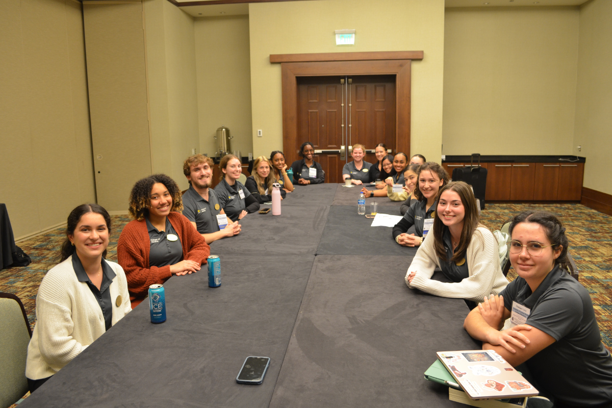 A group of UCF College of Nursing students in business casual attire sit at a conference room table during the 2024 Florida Nursing Students Association convention.