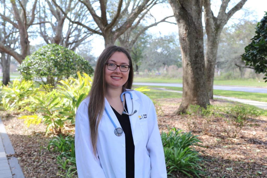 UCF College of Nursing Family Nurse Practitioner student Hailey Glowiak '21BSN smiles in an outdoor courtyard wearing a white clinical coat and stethoscope.