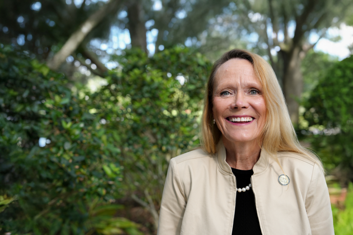Sharon Tucker smiles in an outdoor courtyard. Sharon Tucker, Next Dean of the College of Nursing. UCF Pegasus logo.
