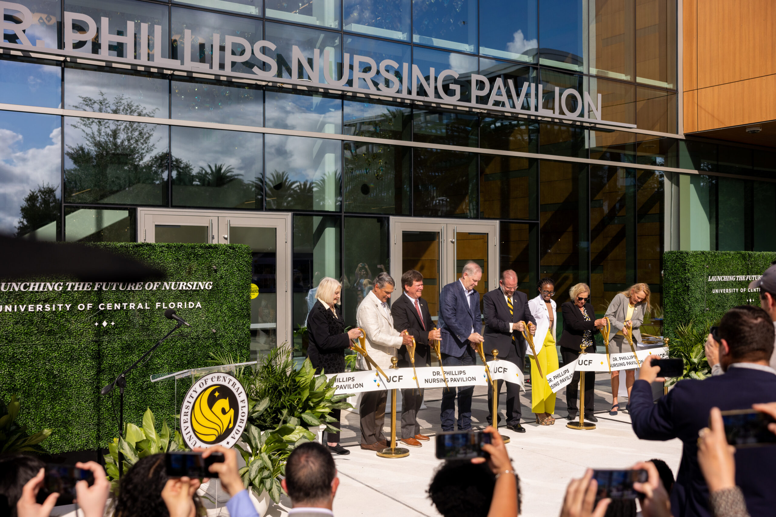Former State Senator Linda Stewart; Alex Martins; Kenneth Robinson, president and CEO of Dr. Phillips Inc. and the Dr. Phillips Foundation; Agriculture Commissioner Winston Simpson; UCF President Alexander N. Cartwright; nursing alumna Nadesha Phipps ’24; Professor Emerita Mary Lou Sole; and College of Nursing Dean Sharon Tucker cutting the ribbon at the Dr. Phillips Nursing Pavilion.