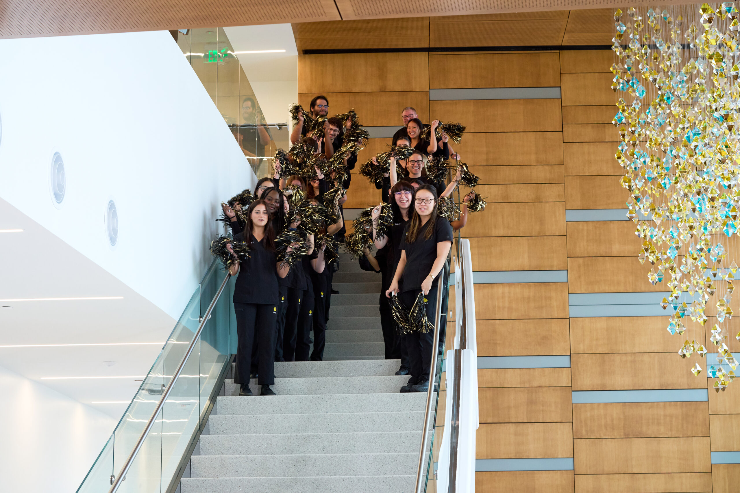 Students standing at the top of the stairs alongside the "Vitality" art piece with pom-poms in hand.