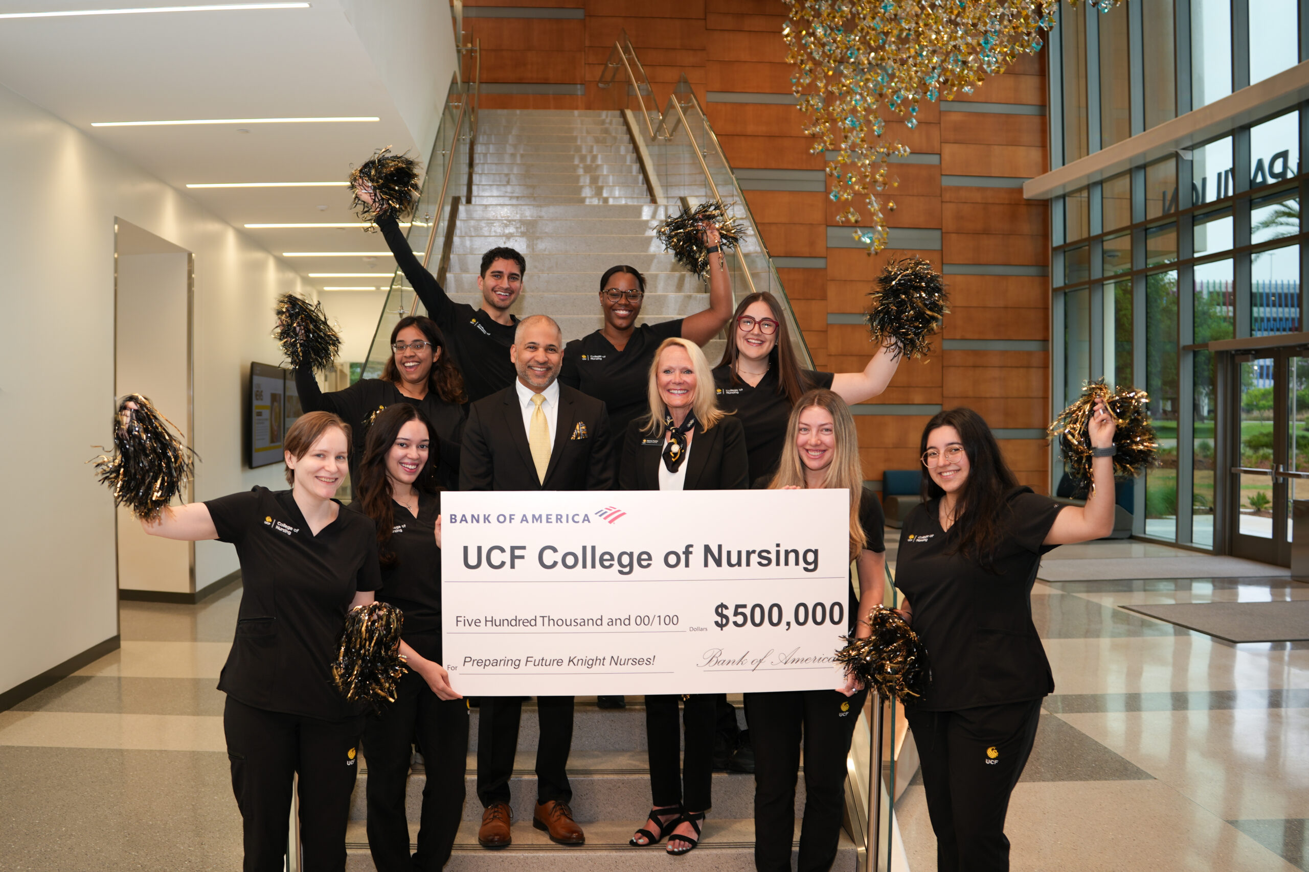 BOA president, Naveed Shujaat and College of Nursing Dean, Sharon Tucker, are smiling around a group of nursing students waving pom-poms in the air. The Bank of America President and College of Nursing Dean are holding a check for 500,000 dollars for "Preparing Future Knight Nurses!"