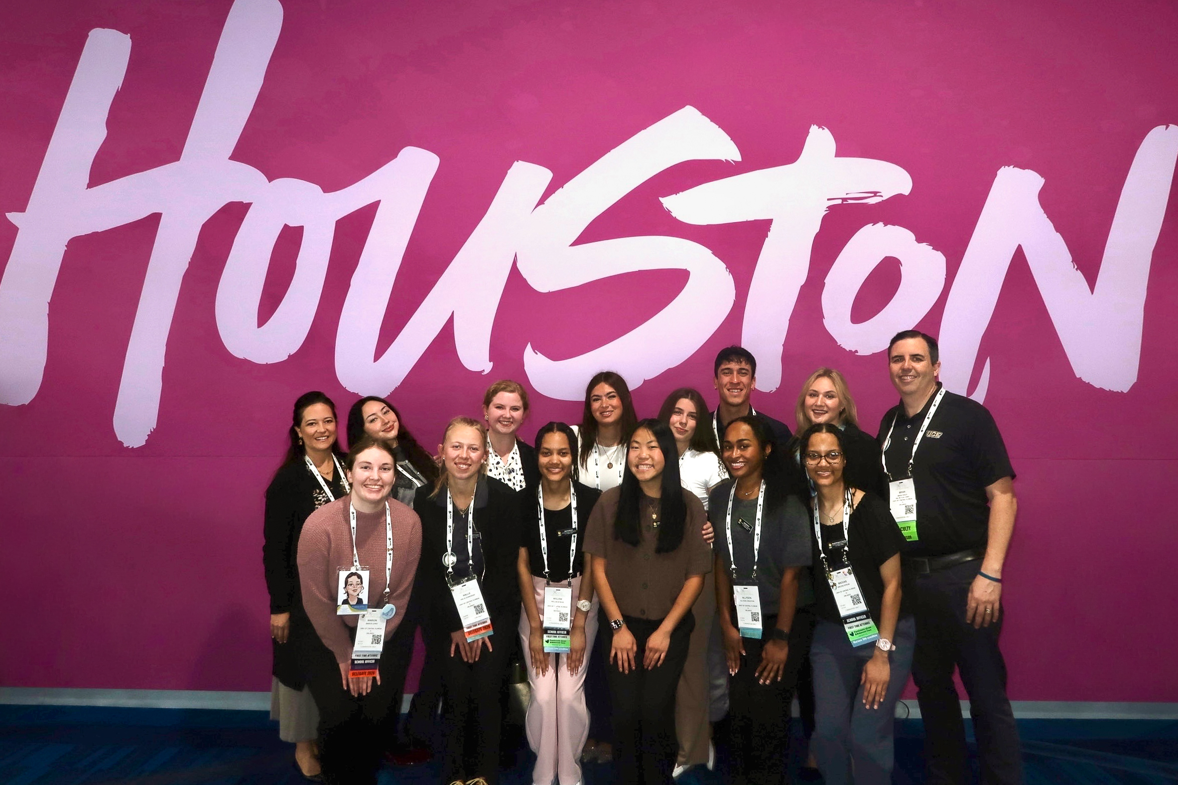 A group of students standing in front of a sign that says "Houston." Alongside with the students are faculty members Kate Dorminy (far left) and Brian Peach (far right).